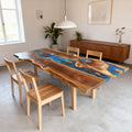 Elegant dining setup showcasing a black walnut blue river epoxy dining table with upholstered chairs and a sleek metal base.